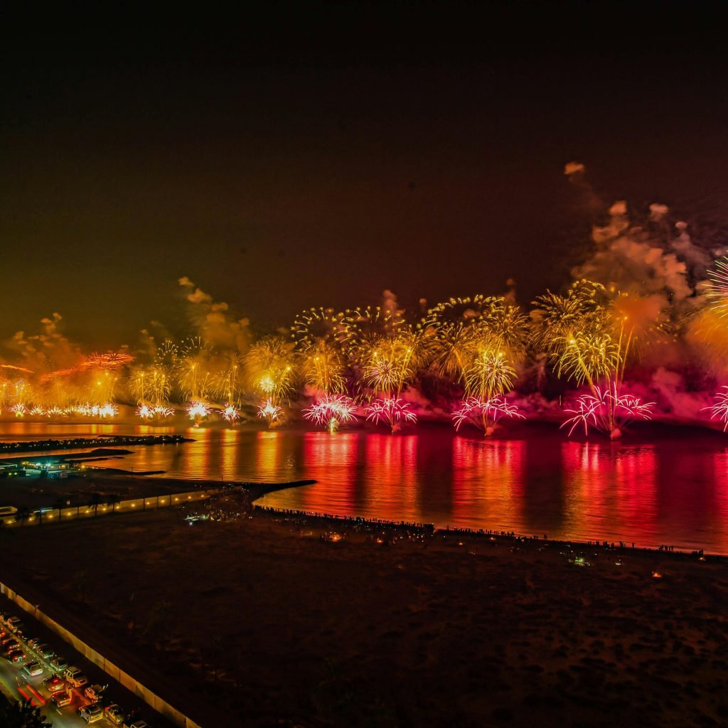 A stunning aerial view of a vibrant fireworks display over the sea in Ras Al-Khaimah at night.