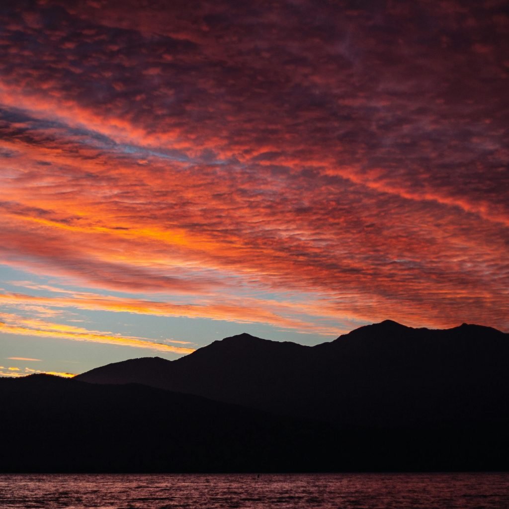 Dramatic sunset sky with vibrant colors over silhouetted mountains and calm water.