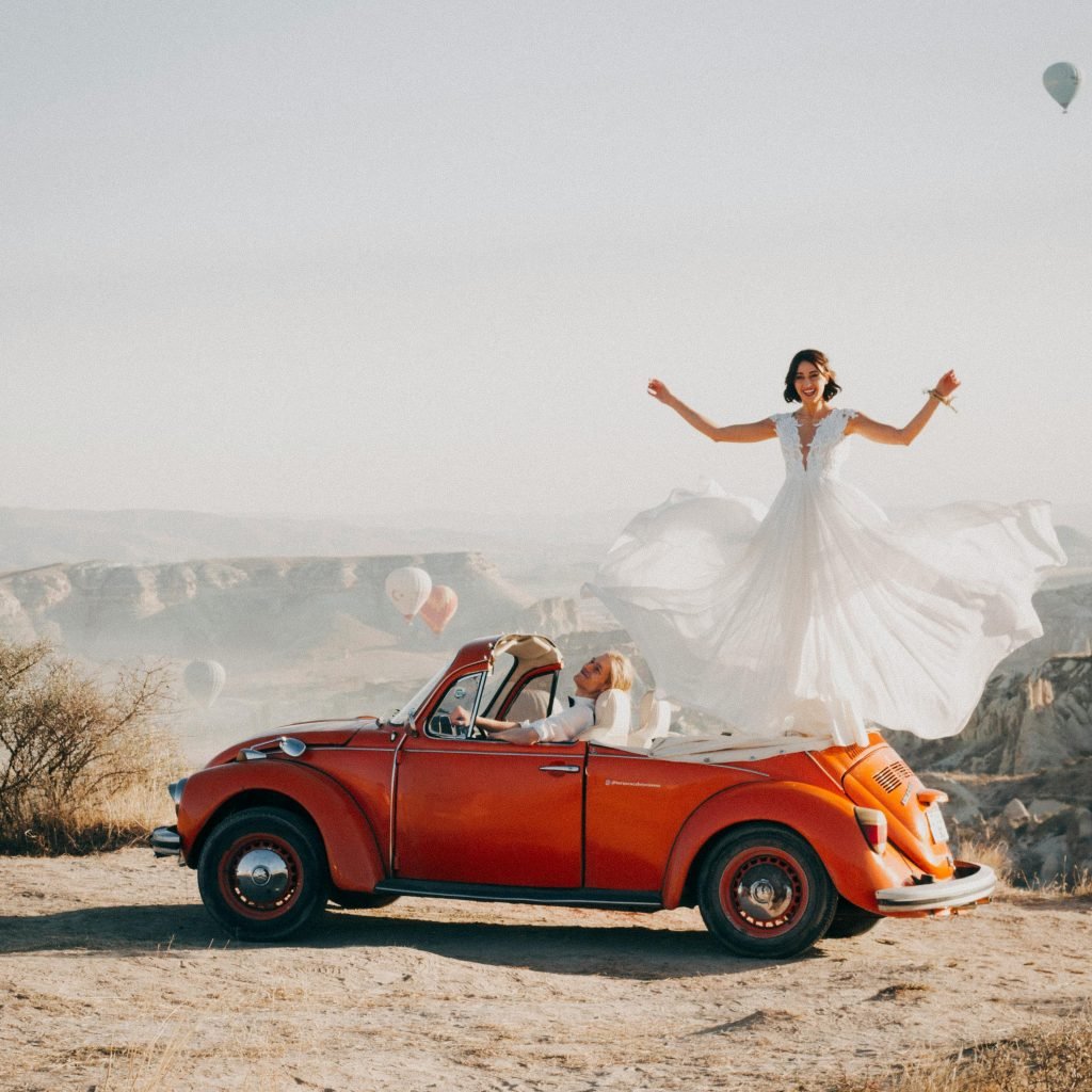 Bride and groom celebrating their wedding atop a vintage car in Cappadocia, Turkey.