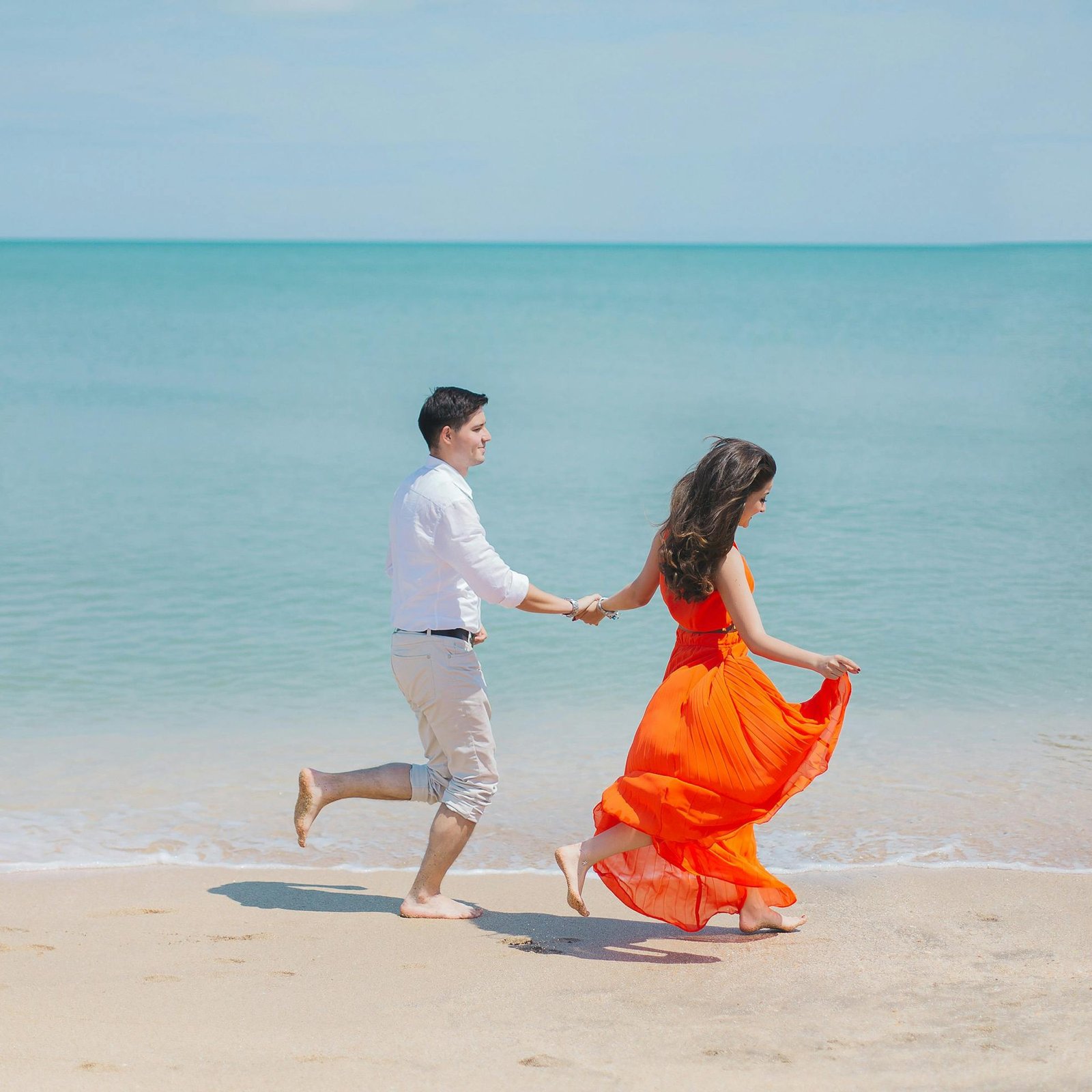 A joyful couple runs barefoot along Baku's sunny coastline, embodying carefree summer love.